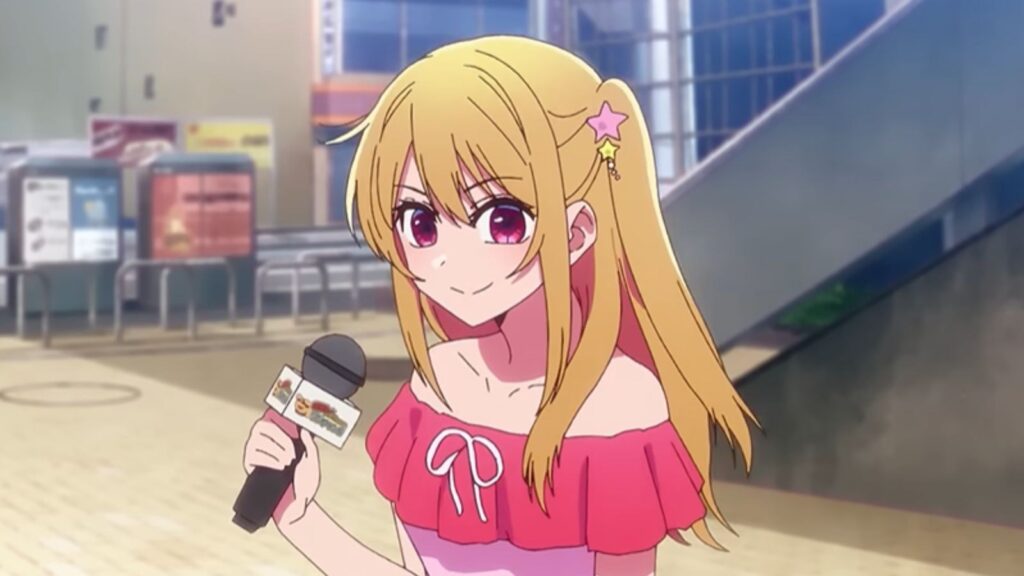 MEM-Cho holding a microphone and smiling during an interview, from Oshi no Ko Season 3