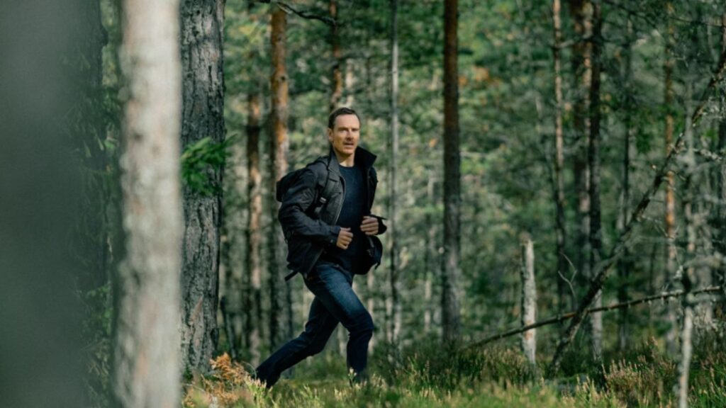 Michael Fassbender running through forest during tense pursuit scene, from The Agency season 1