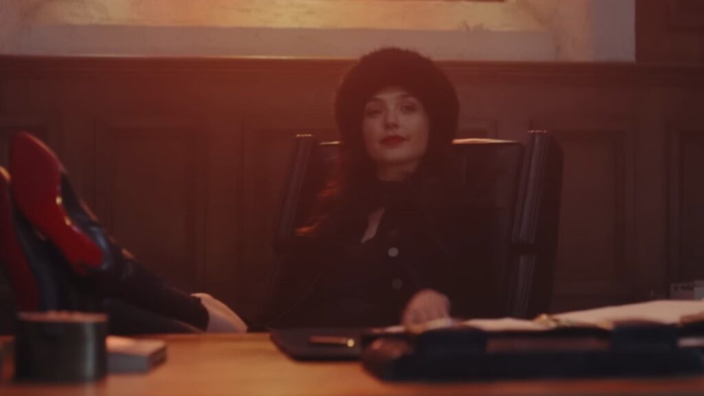 The Bishop lounges behind desk, confident smirk, in Red Notice