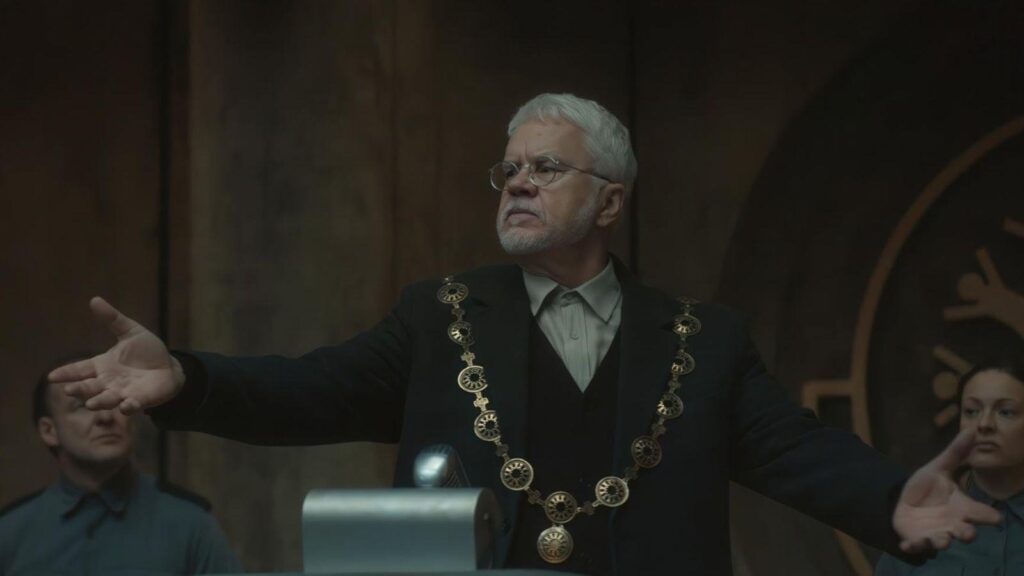 Bernard Holland portrayed by Tim Robbins addressing silo residents in chamber, from Silo season 2