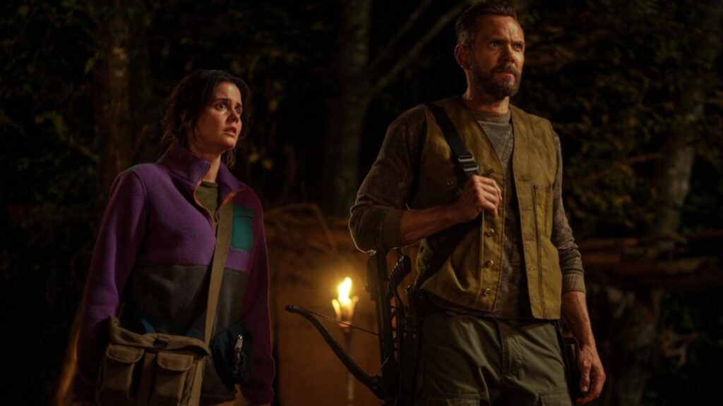 Joel McHale and Ashley Sutton tense nighttime wilderness moment with torchlight, from Yellowjackets season 3