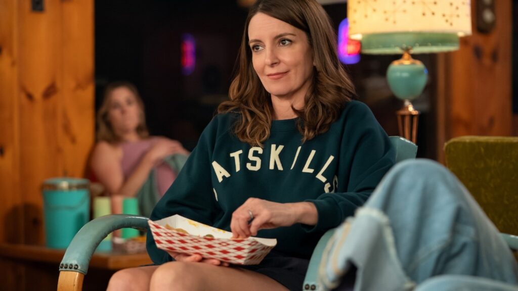Tina Fey sitting thoughtfully indoors holding snacks in The Four Seasons season 2