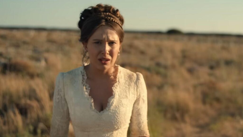 Millie Bobby Brown stands shocked alone wearing wedding dress in Malta, from Enola Holmes 3