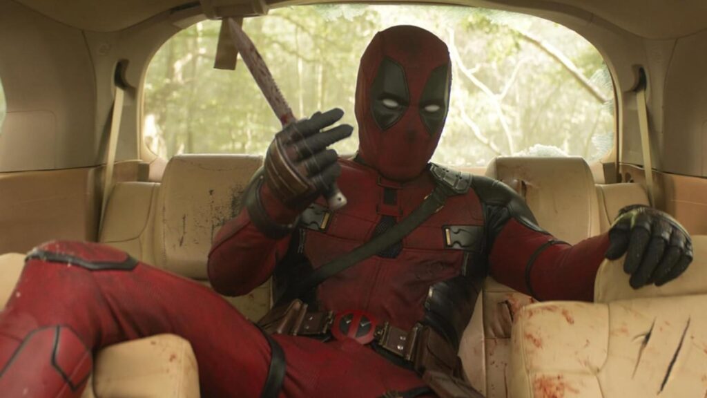 Deadpool relaxes in bloodstained vehicle holding bloody knife after chaotic action sequence in Deadpool 3
