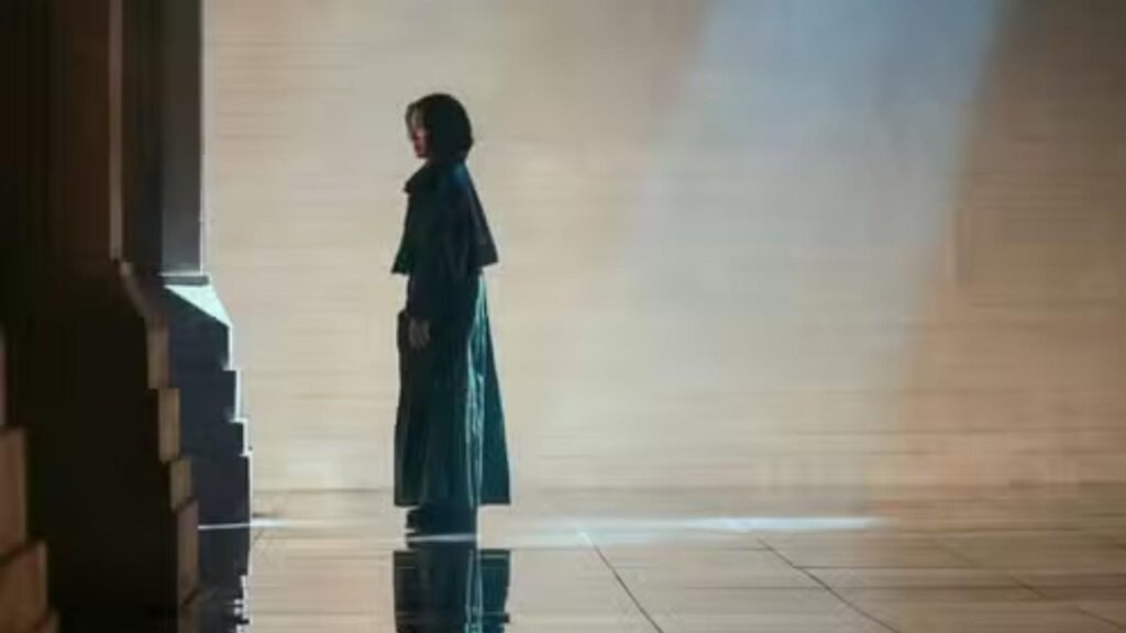 Michelle Yeoh as Olwen stands within expansive futuristic hall illuminated by dramatic beams in Blade Runner 2099