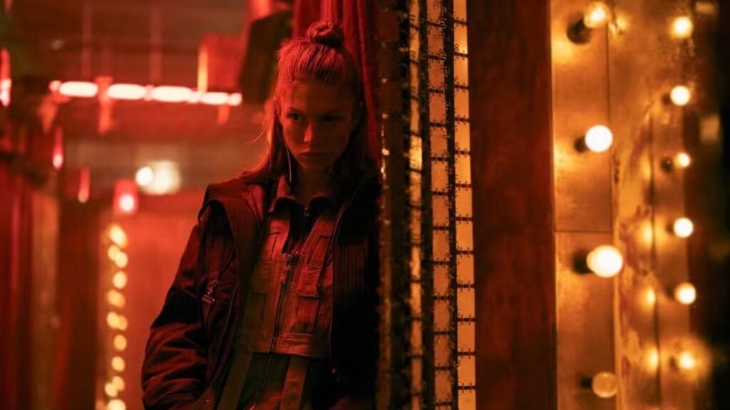 Hunter Schafer as Cora peers around doorway inside neon-lit corridor in Blade Runner 2099