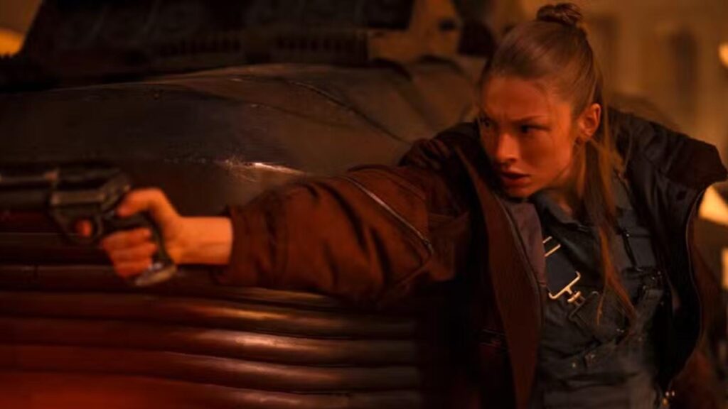 Hunter Schafer as Cora takes cover behind vehicle during intense nighttime confrontation in Blade Runner 2099