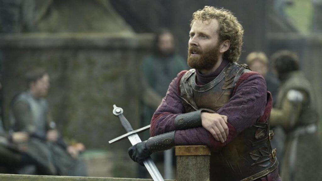 Edward Ashley as Ser Steffon Fossoway leaning on sword in armor awaiting action in A Knight of the Seven Kingdoms