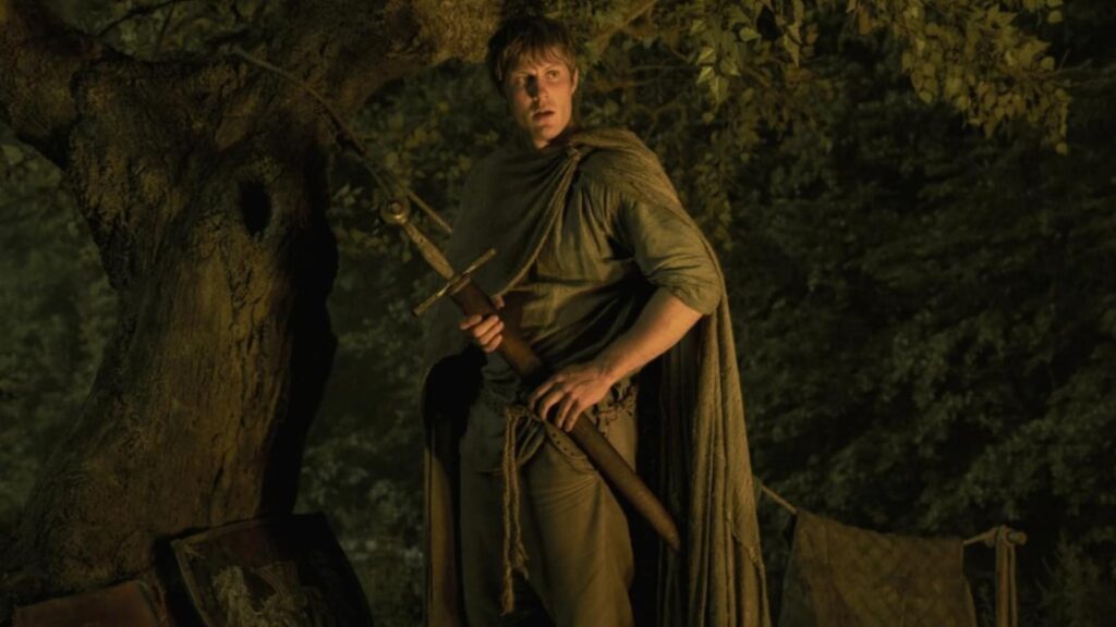 Peter Claffey holding sword beneath forest tree during nighttime scene in A Knight of the Seven Kingdoms
