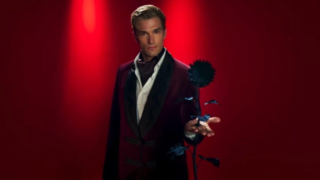 Evan Peters holds black flower against vivid red backdrop, from American Horror Story Season 13