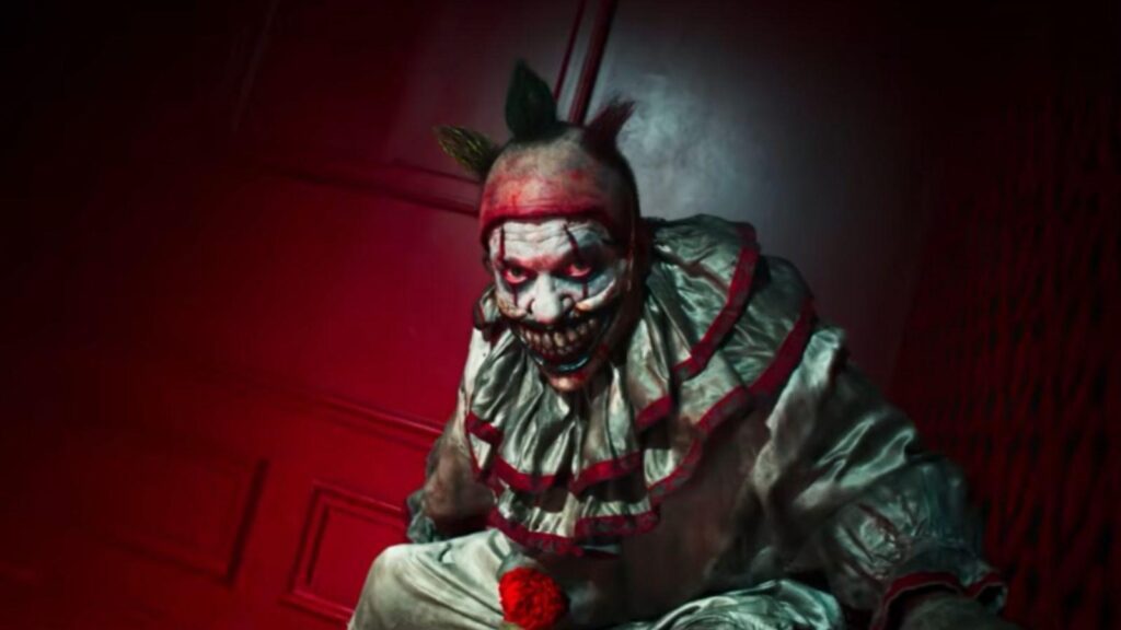 Menacing clown figure crouches inside a red-lit hallway, from American Horror Story Season 13