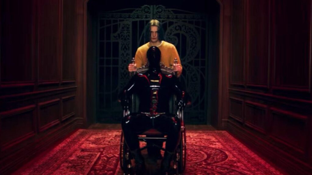 Cheyenne Jackson stands behind seated figure in dark hallway, from American Horror Story Season 13