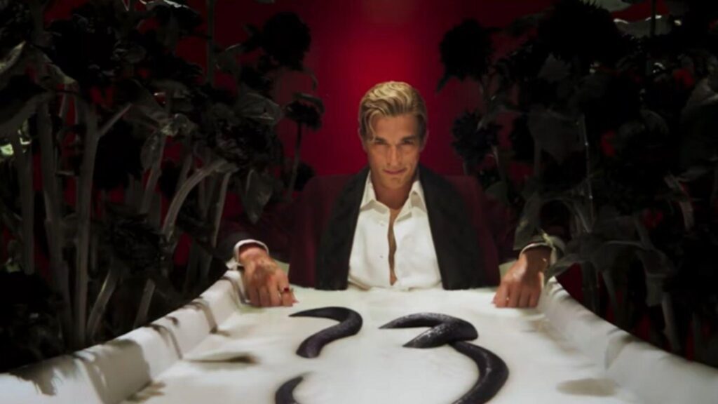 Evan Peters sits beside black flowers and number thirteen, from American Horror Story Season 13