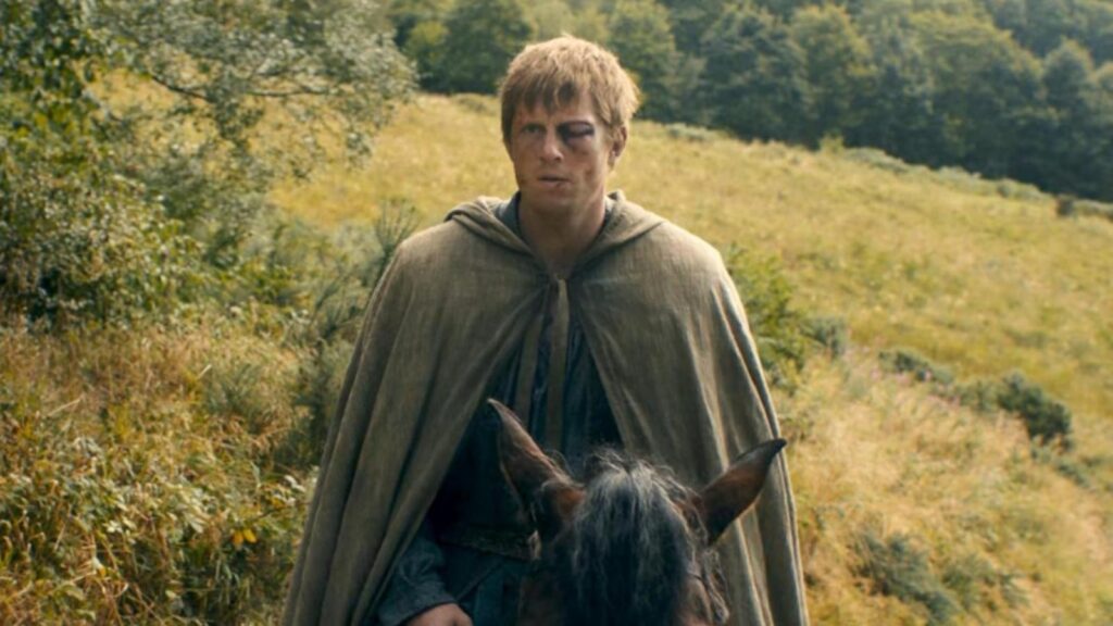 Peter Claffey as Ser Duncan 'Dunk' the Tall wearing a cloak travels horseback through a grassy countryside