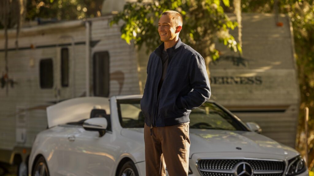 Drew Starkey as Rafe Cameron smiling beside a white convertible and camper in sunlight in Outer Banks season 5