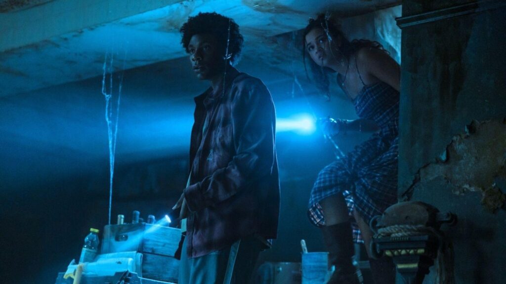 J.D. as Pope Heyward and Madison Bailey as Kiara Carrera searching a dark room with flashlights, from Outer Banks season 5